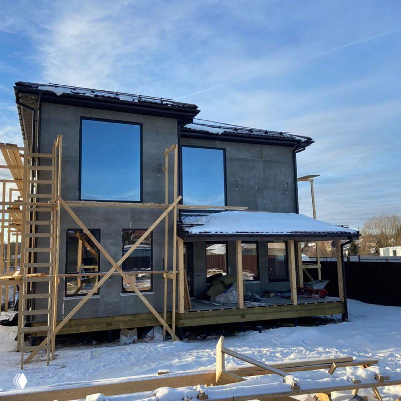 Строящийся частный дом с крупными окнами и лесами снаружи — пример этапа монтажа остекления фасада зимой.
