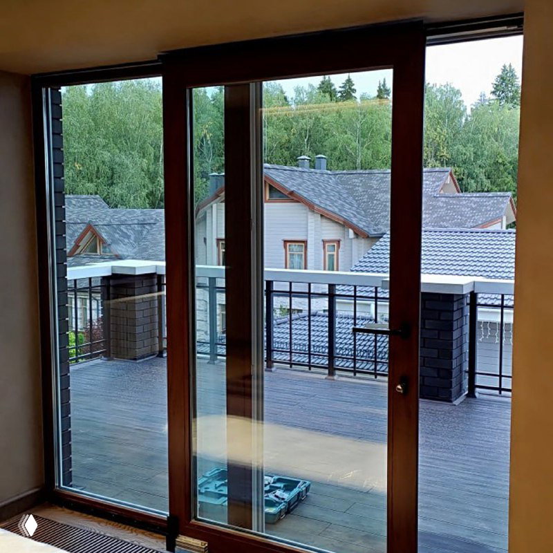 Раздвижная террасная дверь из дерева или тёмного профиля, ведущая на балкон — пример уличного выхода с большими стеклянными поверхностями.