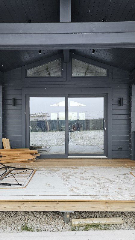 Тёмная раздвижная дверь с верхними трапециевидными вставками остекления на террасе; ракурс показывает облицовку и покрытие террасной доски.