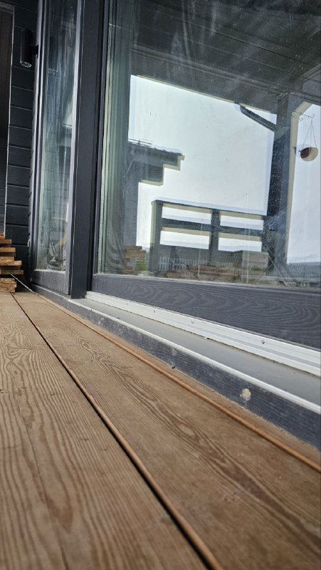 Крупный план порога и нижней части раздвижной системы, видна герметизация стыка и деревянная террасная доска с остатками снега.