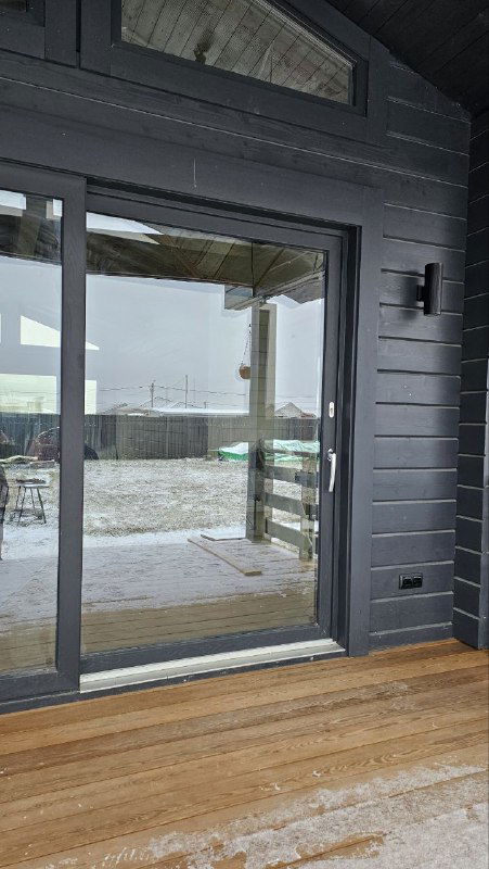 Рефлективная поверхность стекла раздвижной двери, отражающая участок участка и дом; вид на ручку и сторону открывания.