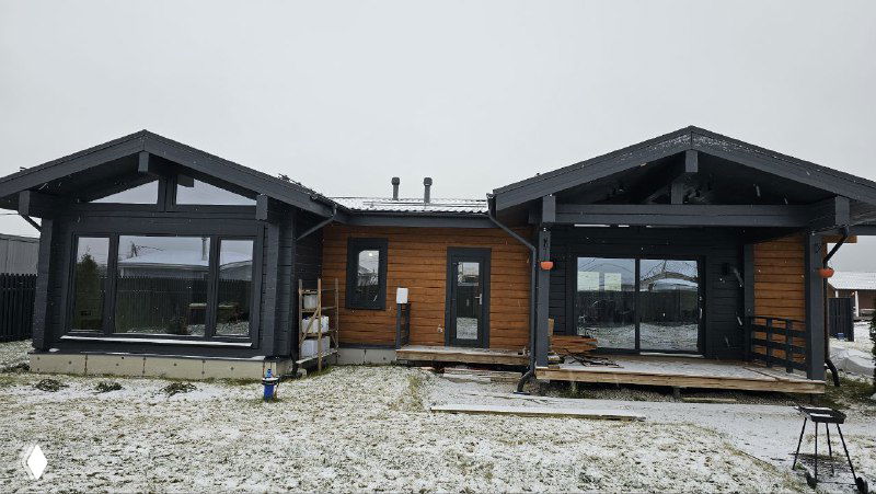 Панорамный вид фасада деревянного дома с несколькими большими остеклёнными проёмами и установленной раздвижной дверью в центральной части.