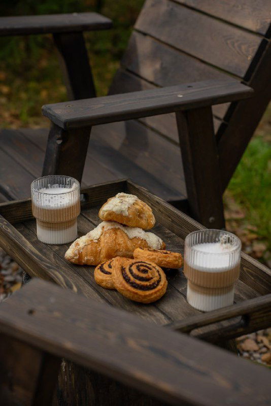 Крупный план стола на террасе с круассанами и двумя стаканами латте, создающий ощущение уюта и гостеприимства у панорамных окон дома.