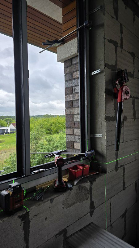 Окна GEALAN S9000 в процессе монтажа: внутренняя сторона проема из газобетона, лазерный нивелир и инструменты на подоконнике.