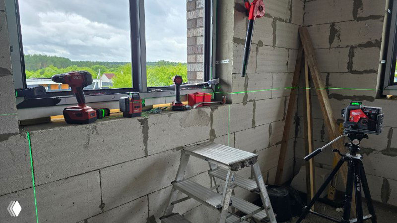 Широкий кадр рабочего проема с инструментами, лазерной линией и подготовленным подоконником — видна внутренняя кладка газобетона.
