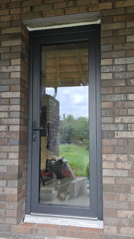 Установленная дверь с темной ламинацией на внешней кирпичной облицовке — демонстрация цветового решения антрацит и внешней плитки.