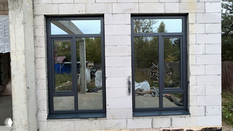 Наружный вид установленного окна в газобетонном доме: серый антрацит, панорамные створки, монтажный проём и строительная площадка вокруг.