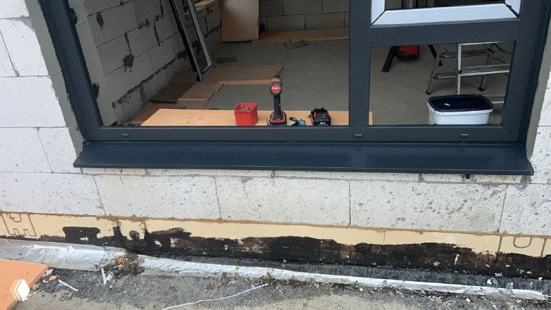 Ближний план нижней части оконного проёма с отливом и подготовленной зоной монтажа; видно места герметизации и прилегания к несущей стене.