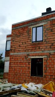 Фасад из керамических блоков с несколькими оконными проёмами: видны установленные рамные блоки, пустые отверстия и строительный мусор у фундамента, иллюстрация ошибок монтажа