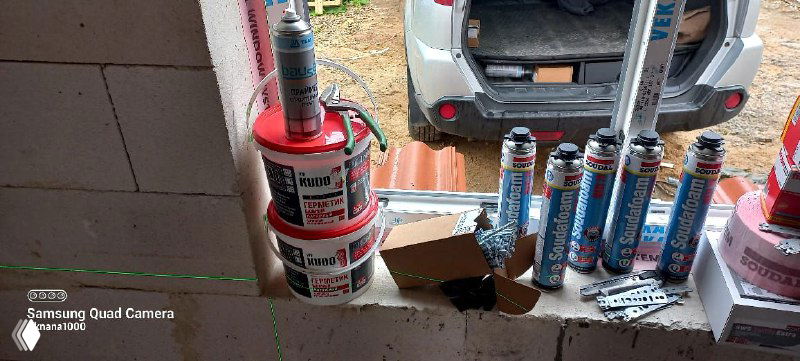 Строительные материалы и инструменты на подоконнике и в багажнике автомобиля: ленты, герметики и банки монтажной пены для остекления.