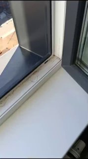 Крупный план угла пластикового окна: рама, подоконник и откос, показывающие следы установки и возможные проблемы при слабом армировании