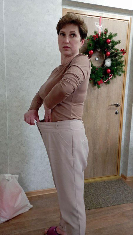 Фотография той же ученицы в тех же брюках, показывает свободный пояс рукой — визуальное подтверждение потери веса и эффекта домашних тренировок