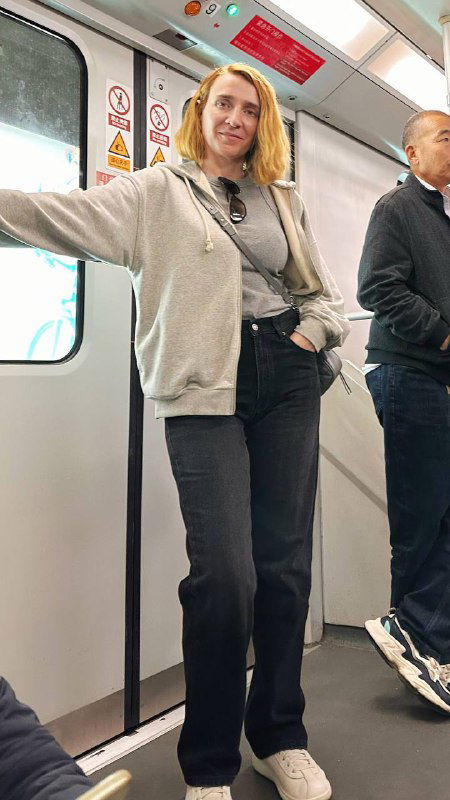 Салон поезда Шанхайского метро: стоящая женщина держится за поручень, другие пассажиры, интерьер вагона и обычная поездка по линиям города.