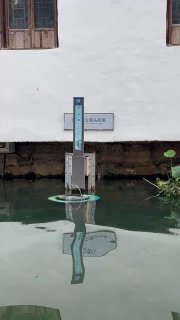 Отражение информационного указателя и белого фасада дома в спокойной воде узкого канала старого китайского города, тихая рефлексия на воде.