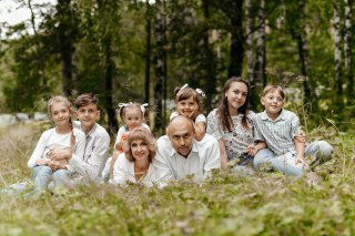 Групповая фотография семьи: родители и шестеро детей на природе, улыбаются и сидят в траве — иллюстрация истории о награде.