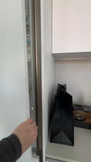 Деталь кухни: открывается узкий шкаф с видом на черный подарочный пакет на рабочей поверхности, видна рука и элементы кухни вокруг.