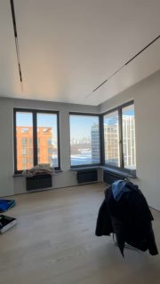 Гостиная с большими окнами и видом на город: светлый пол, панорамные стекла, незаконченная расстановка вещей и ощущение нового пространства.