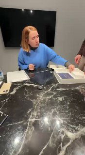 Олеся рассматривает документы и коробку с бумагами на том же столе: рабочий момент оформления, обсуждение деталей и контроль бумаг.