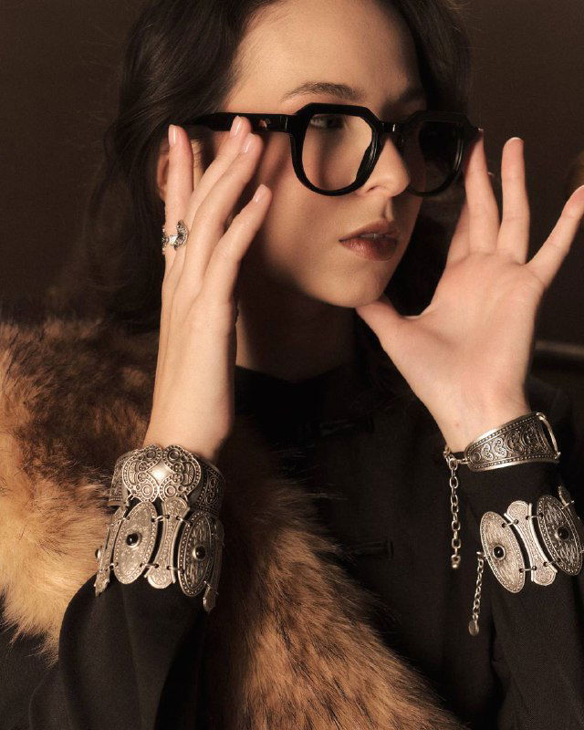 Крупный план рук и украшений рядом с очками: детализированная оправа и авторские аксессуары в ретро-стилистике фотосессии.