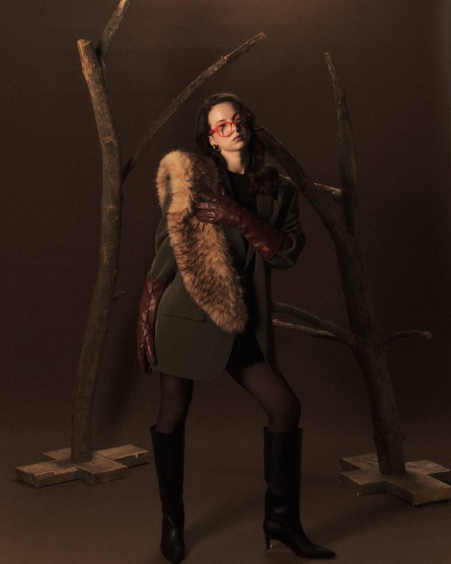 Полный рост модели в очках коллекции «Сунгирь», шубный элемент и ветви создают образ, отсылающий к археологической эстетике.