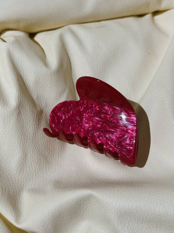 Ярко-малинового цвета крабик из полупрозрачного ацетата на светлом тканевом фоне, подчёркивающий игру света в материале.