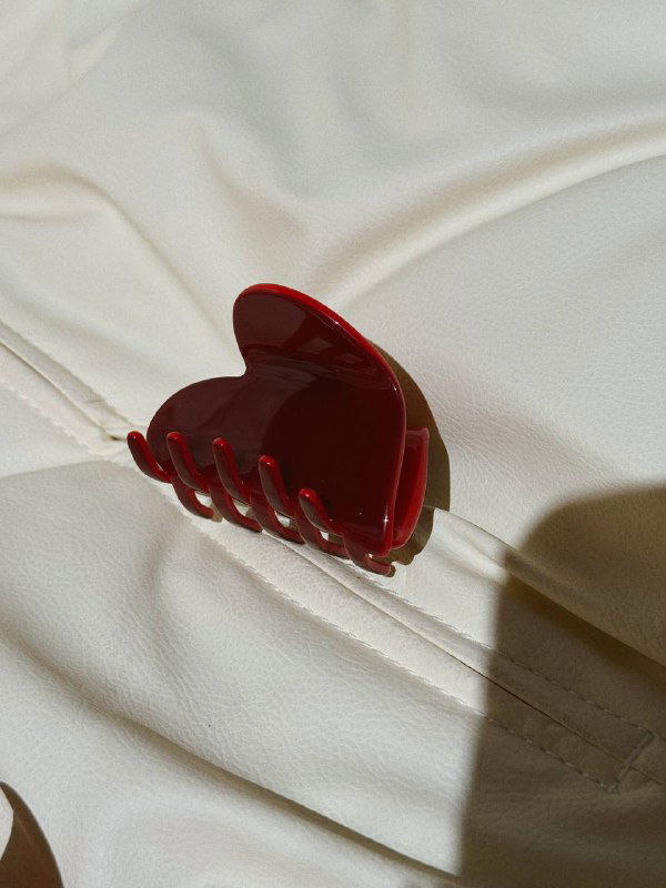 Глянцевый красный крабик на кремовой ткани, освещение подчёркивает гладкую поверхность и контуры аксессуара.