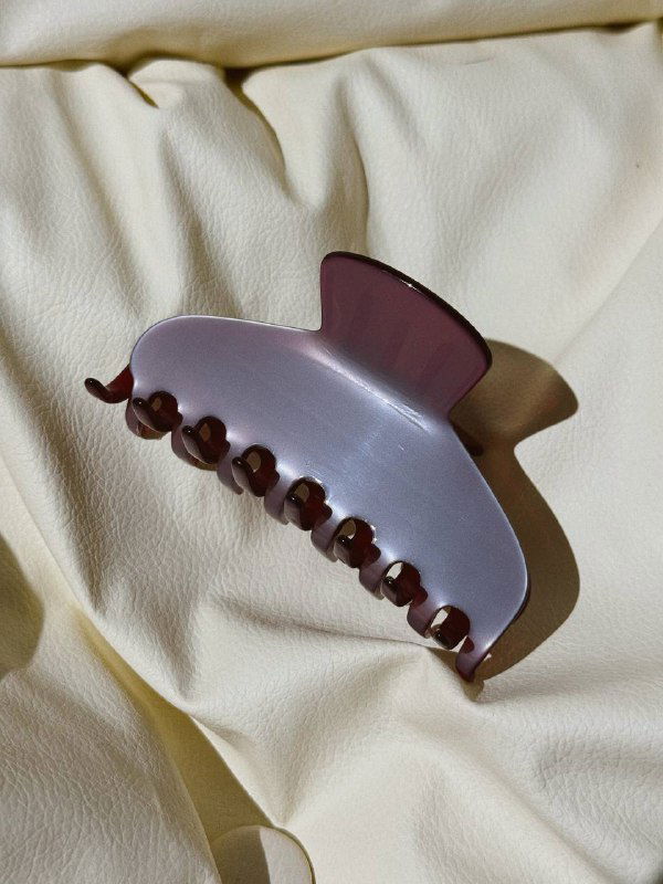 Пастельно-лиловый полупрозрачный крабик из ацетата, сфотографирован на мягкой складчатой ткани в естественном свете.