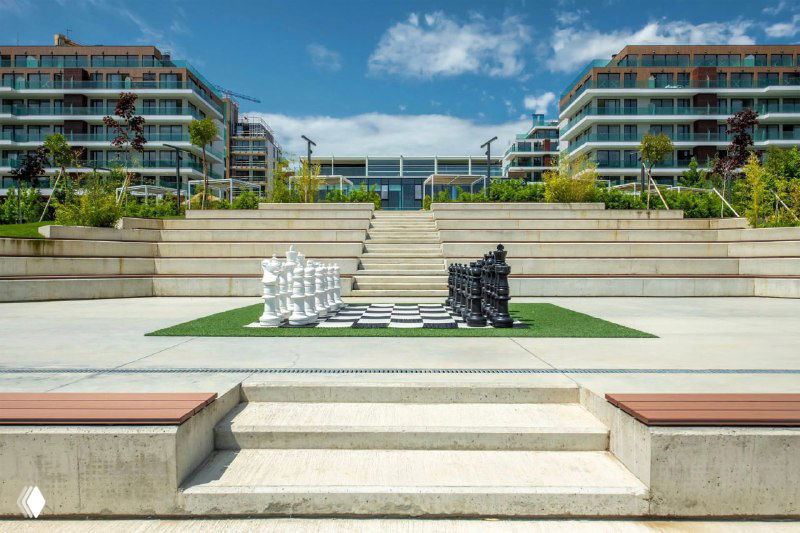 Открытая прогулочная зона с гигантской шахматной доской между жилыми корпусами и террасами — благоустроенный двор комплекса.