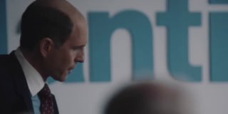 Крупный план мужчины в костюме на фоне размытых букв на постере — кадр из сцен биографического фильма о BlackBerry и корпоративной конкуренции.