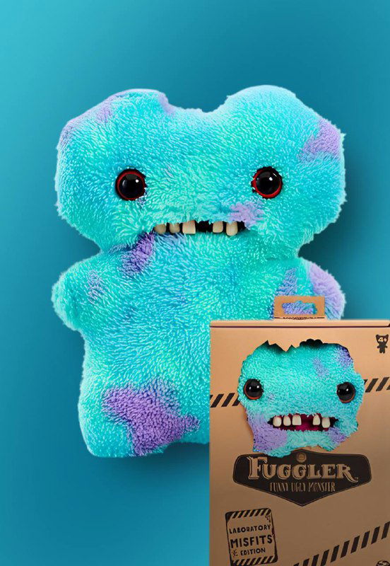 Пастельно-голубой плюшевый Fuggler с тёмными глазами и зубами в упаковке на однотонном фоне, продуктовый снимок крупным планом