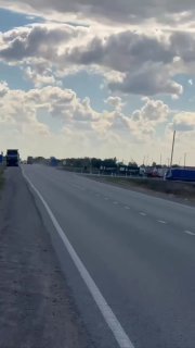 Длинная автомобильная трасса у приграничной зоны на фоне плотных облаков; видны фуры вдалёке и дорожная обстановка.