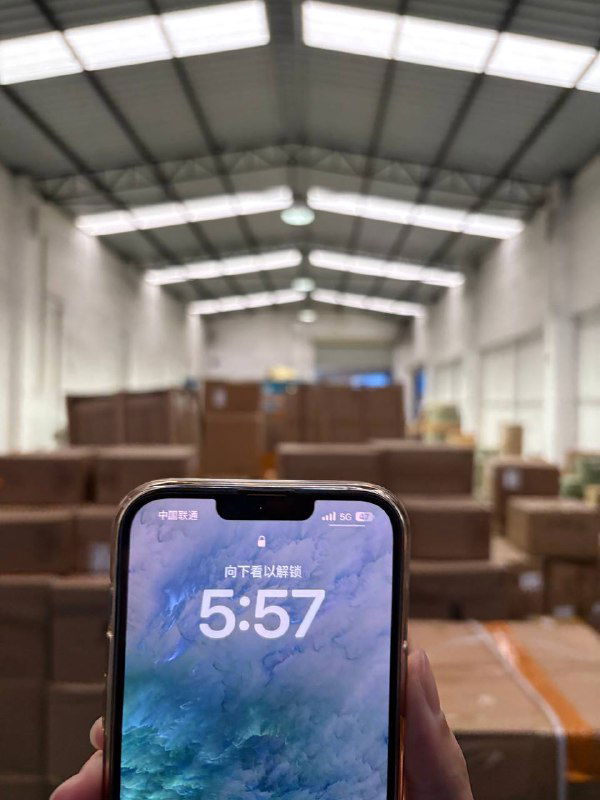 Рука держит смартфон с видимым временем на фоне рядов коробок внутри склада Panda28 — рабочая сцена упаковки и учёта.