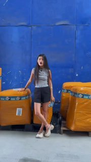 На фото девушка стоит рядом с упакованными паллетами и крупными жёлтыми упаковками в складском помещении на синем фоне — иллюстрация логистического кейса.