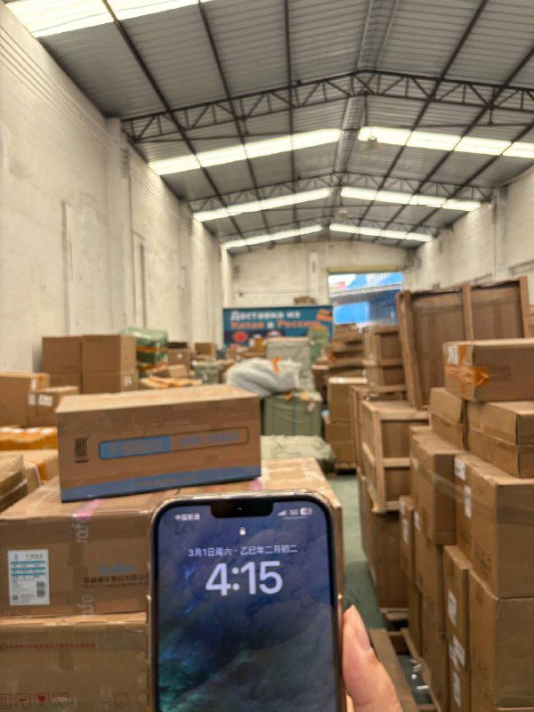 Камера показывает внутреннюю часть склада Panda28 с множеством коробок и паллет; на переднем плане держат смартфон с временем на экране.