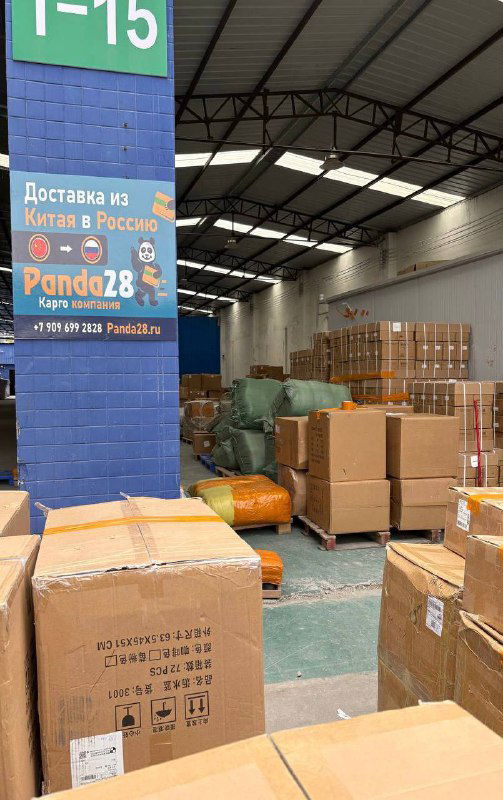 Крупные картонные коробки и мешки внутри склада Panda28 рядом с колонной, на колонне размещена рекламная панель компании с контактами.