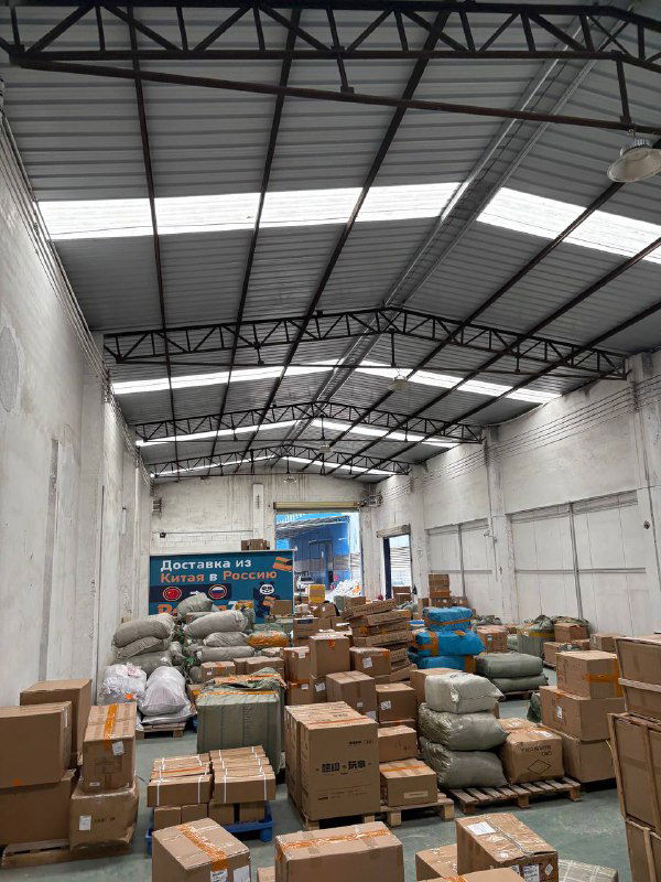 Ярко освещённый склад Panda28, полки не видны, но в проходе аккуратно размещены стопки коробок и сумок для логистической обработки.