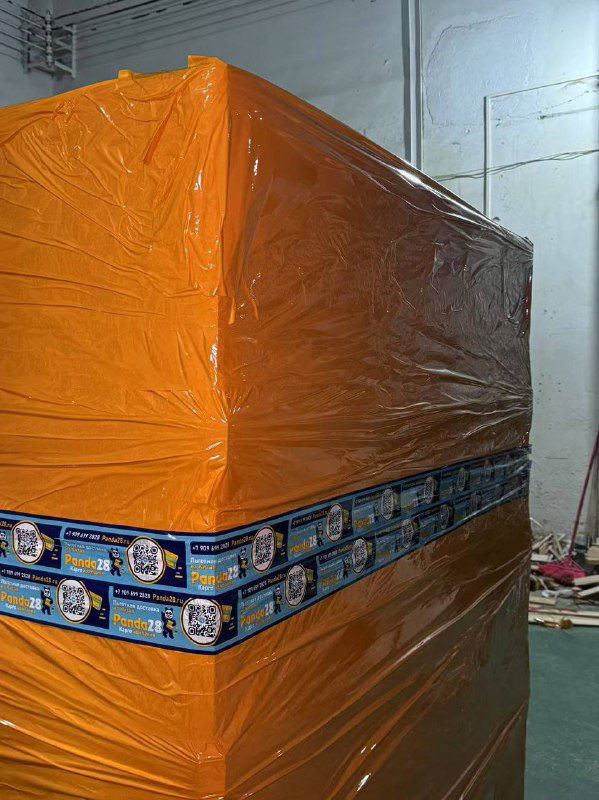 Упакованный крупногабаритный груз, обёрнутый в оранжевую плёнку с брендированной лентой Panda28, готов к погрузке в контейнер.