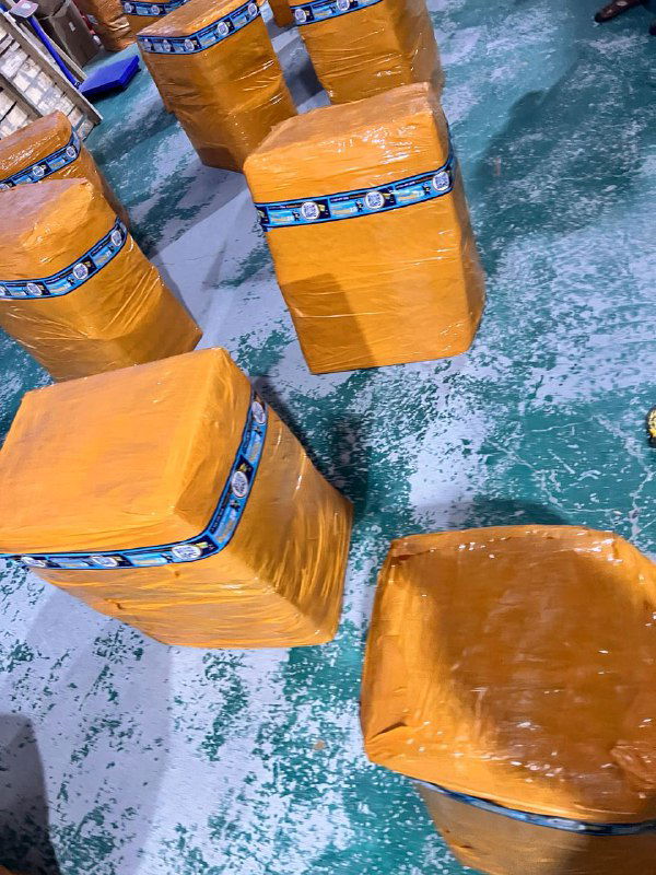 Несколько оранжевых упакованных посылок на зелёном бетонном полу склада, подготовленные к консолидации и отправке в Россию.