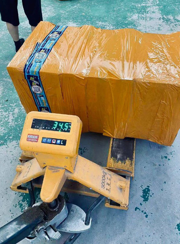 Упакованная жёлтая коробка на весах-паллетнике: цифровое табло показывает значение веса, демонстрируя точный процесс взвешивания.
