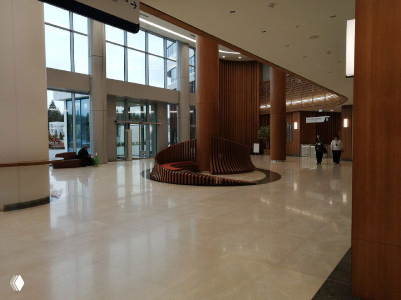 Просторный холл медицинского центра с высокими окнами, светлым полом и деревянными колоннами — вид изнутри приёмной зоны.