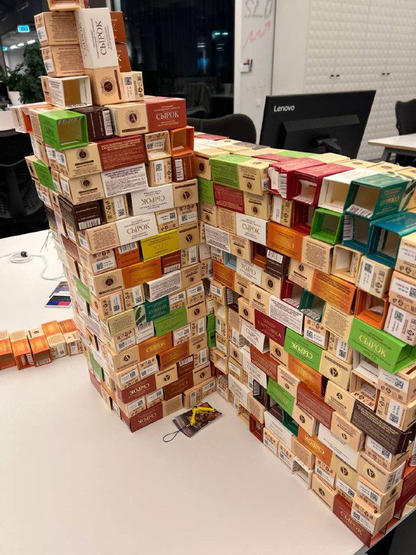 Две высокие стопки пустых упаковок сырков на рабочем столе в офисе, снято ночью; демонстрация распределения популярных вкусов среди сотрудников.