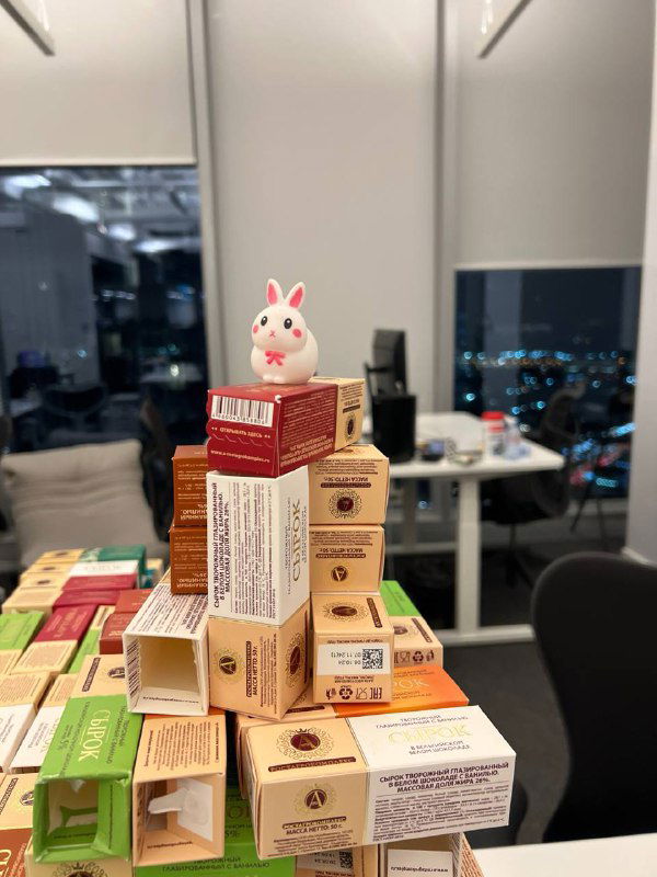 Крупный план верхушки башни из упаковок сырков с маленькой игрушкой на вершине — игровая физикализация статистики о предпочтениях персонала.