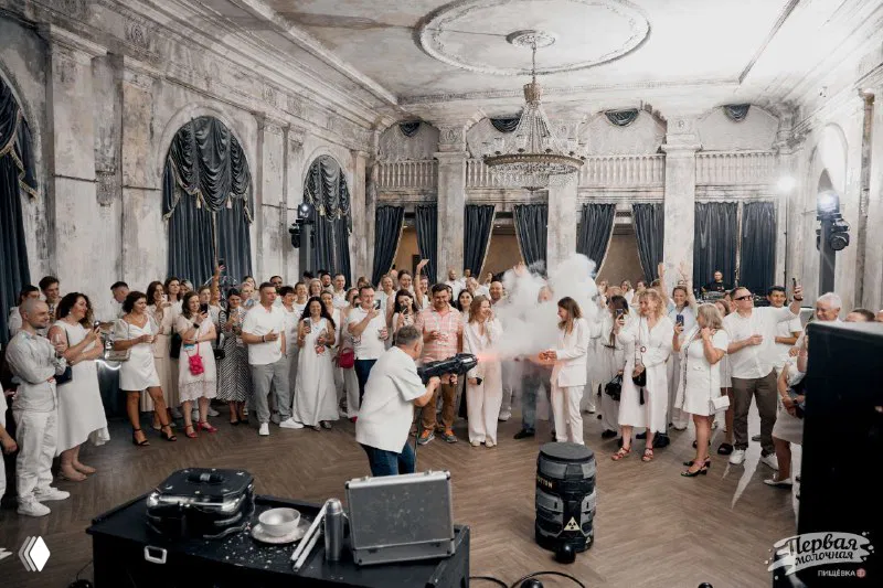 Гости на вечерней белой вечеринке в историческом зале Петербурга: танцы, люди в белом дресс-коде, сцена и праздничная атмосфера.