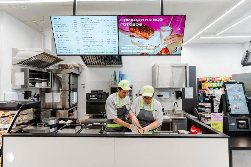 Рабочая зона кухни в магазине: персонал в форме готовит блюда на месте, видны плиты, раменоварка и профессиональное оборудование для приготовления ready-to-eat.