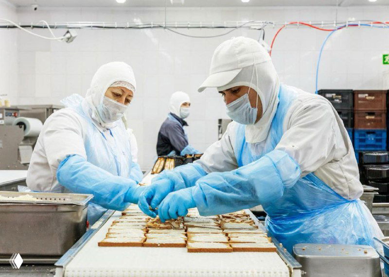 Производственная линия Mr.Food: сотрудники в санитарной форме, перчатках и масках формируют готовые блюда на конвейере в цехе пищевого производства.