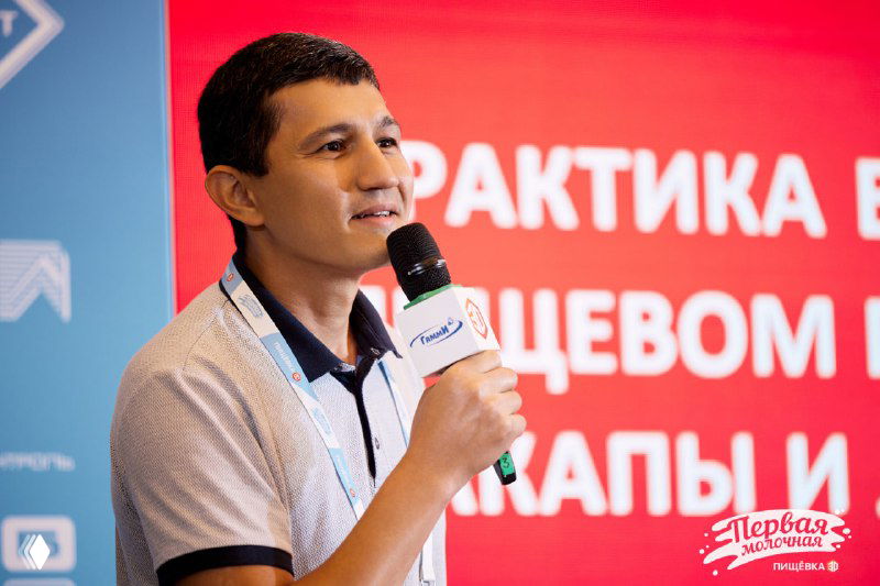 Спикер ЛПР держит микрофон на сцене конференции, крупный план выступающего на фоне красного слайда с заголовком и брендом.