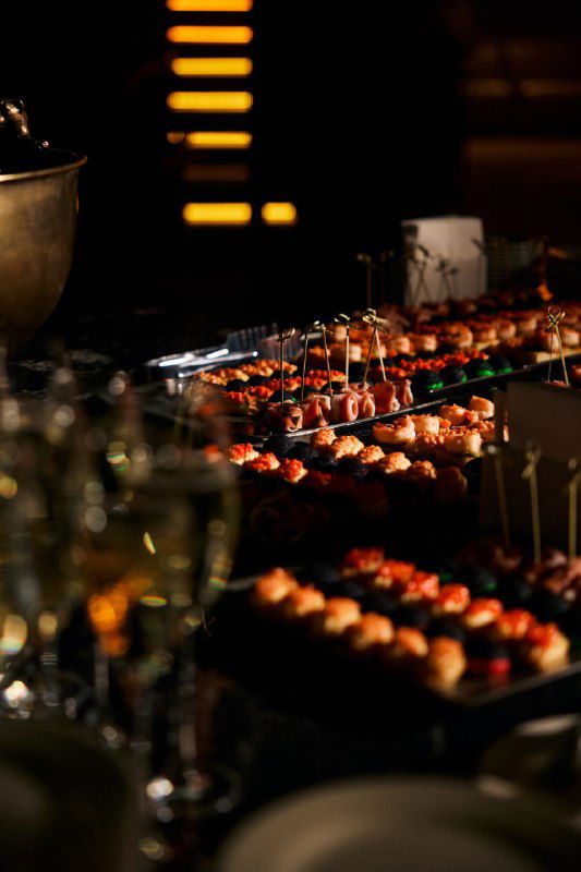 Кейтеринг и канапе в фокусе на фоне приглушённого света: закуски, сервировка и элементы фуршета для гостей Meat Night в зале мероприятия.