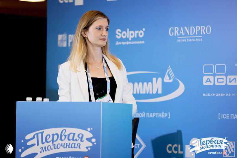 Оратор у трибуны на фоне баннера «Гамми» и «Первая молочная», кадр с презентации продуктовых решений и обсуждения отраслевых тем.