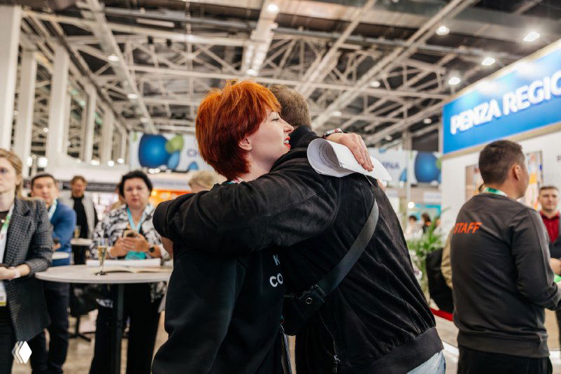 Тёплая встреча и объятия между участниками конференции на выставочной площадке, кадр передавший дружелюбную атмосферу мероприятия.