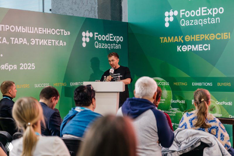 Докладчик на сцене FoodExpo Qazaqstan ведёт презентацию перед аудиторией; на фоне — зелёный баннер выставки и логотипы организаторов.